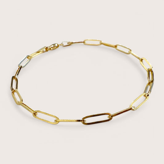 A close up of a 14K gold paperclip bracelet with interlinked elongated chain and a lobster clasp closure.