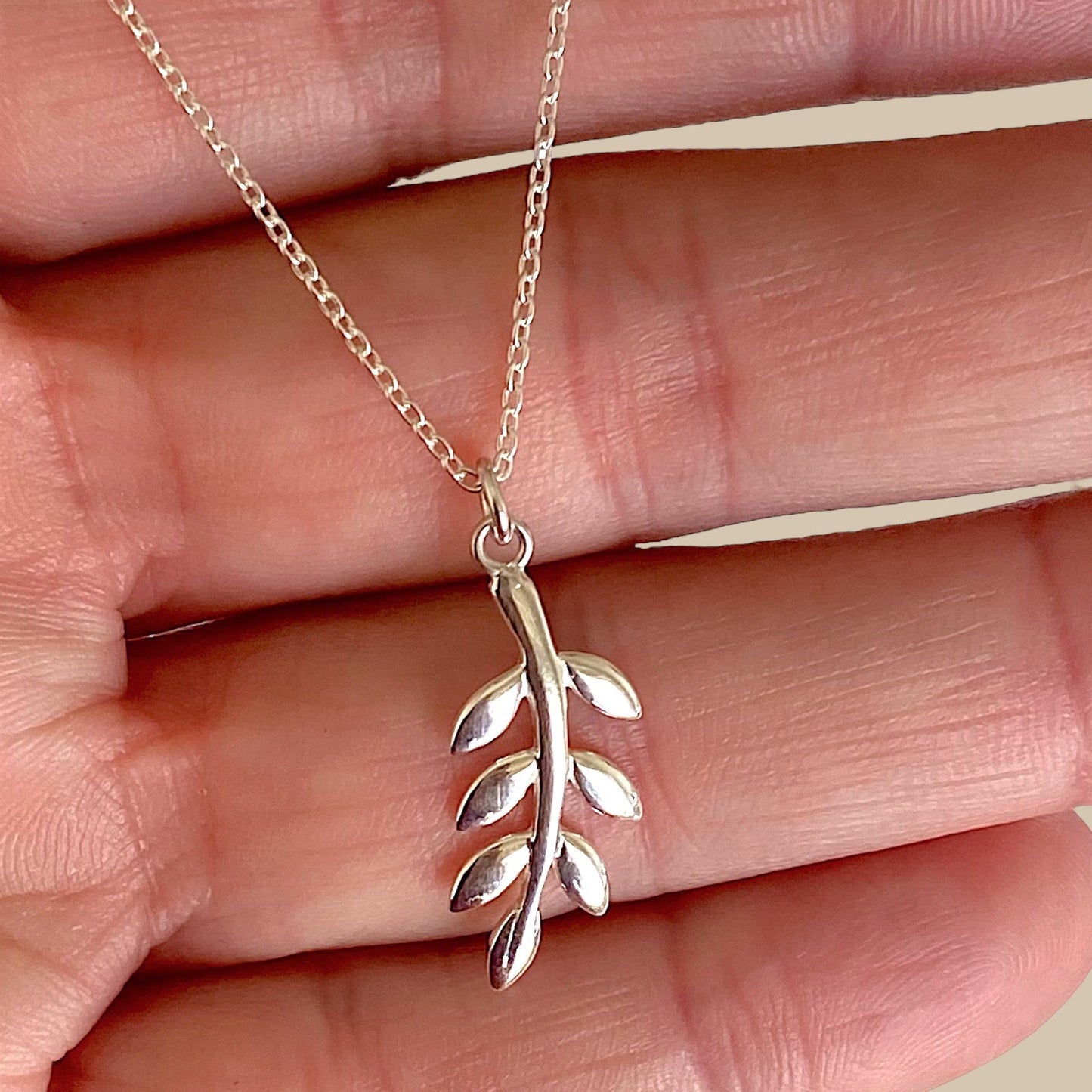 A close up image of a branch pendant necklace held in a hand made in solid 925 sterling silver with a delicate cable chain
