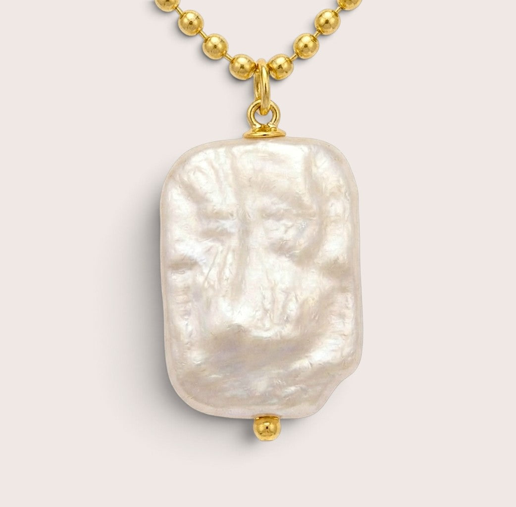Close-up of a rectangular freshwater pearl pendant showing its uneven nacre texture, gold bail, and small gold bead beneath.