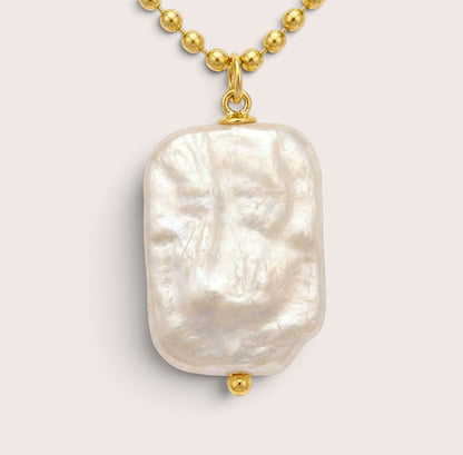 Close-up of a rectangular freshwater pearl pendant showing its uneven nacre texture, gold bail, and small gold bead beneath.