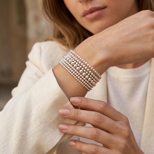 Stacked sterling silver bead bracelets worn on a wrist with an ivory linen sleeve
