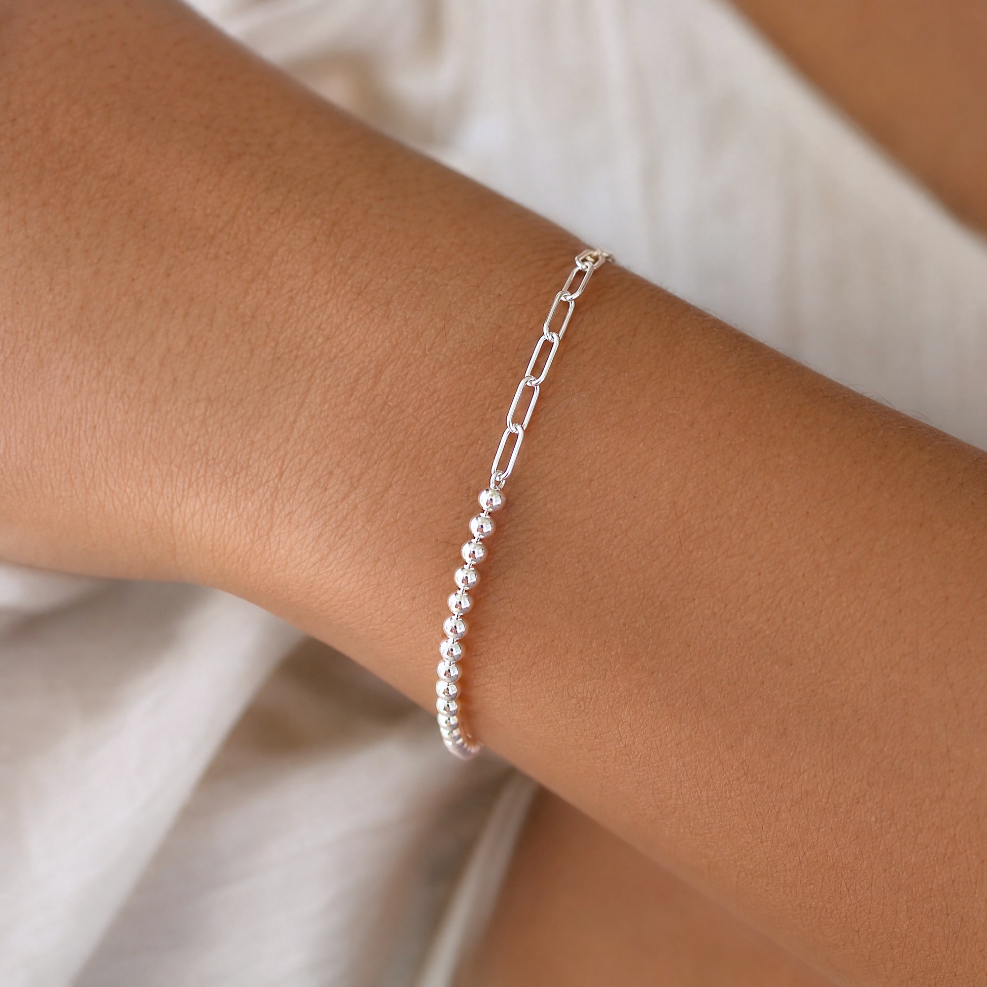 A model wearing the Italian mixed link sterling silver bracelet on a wrist, demonstrating how the asymmetric paperclip chain and 3mm silver beads drape when worn.