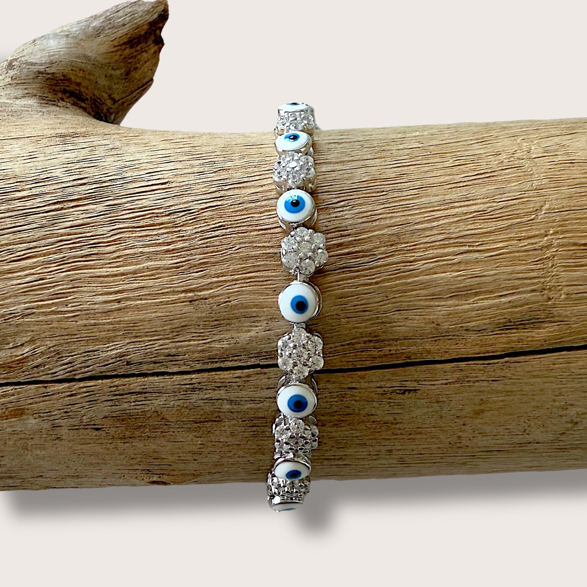 Close up of  sterling silver bracelet featuring a dark blue evil eye and clusters of clear cubic zirconia stones.