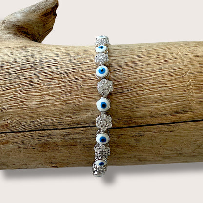 Close up of  sterling silver bracelet featuring a dark blue evil eye and clusters of clear cubic zirconia stones.