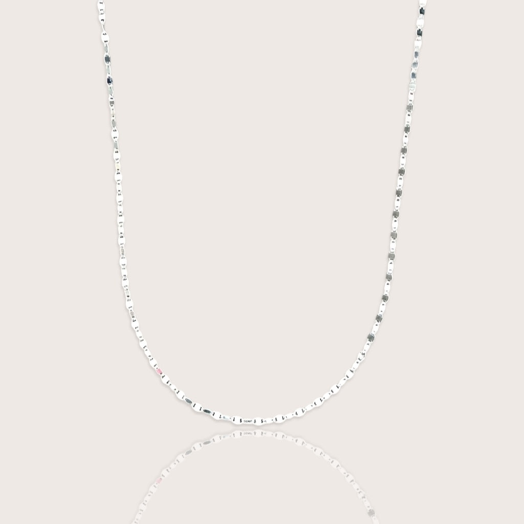 A shimmering silver neckline layer featuring the Ashley Nicole Jewelry flat mirror link chain catching the light on a model.