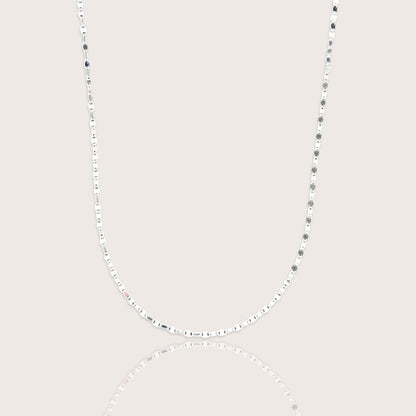 A shimmering silver neckline layer featuring the Ashley Nicole Jewelry flat mirror link chain catching the light on a model.