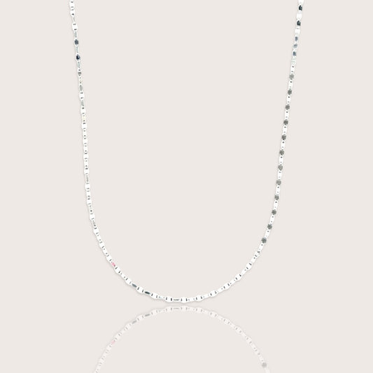 A shimmering silver neckline layer featuring the Ashley Nicole Jewelry flat mirror link chain catching the light on a model.