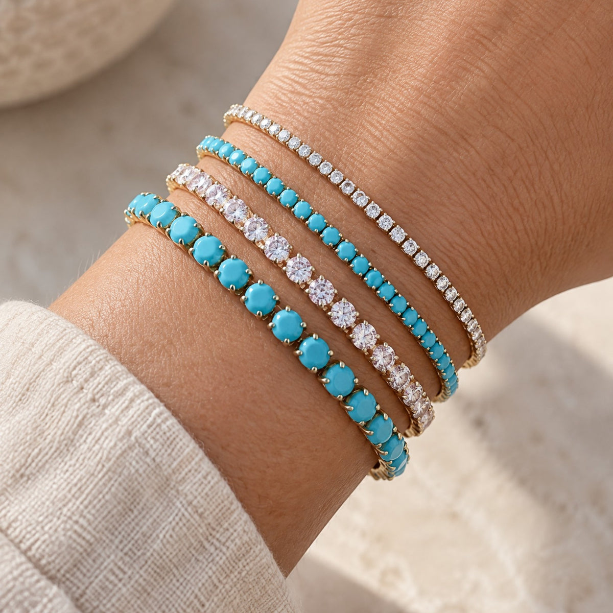 Model wearing a waterproof gold turquoise tennis bracelet layered with other gold chain stacks.