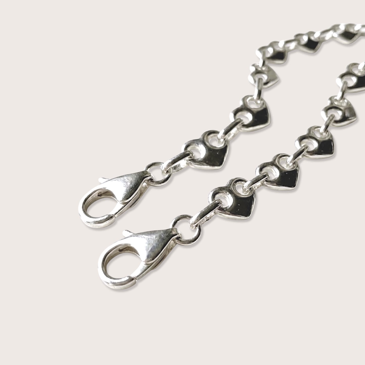 A close up image of a chunky solid silver puffed heart mariner bracelet on a plain background focused on the lobster clasp closure and the heavy weight link chain