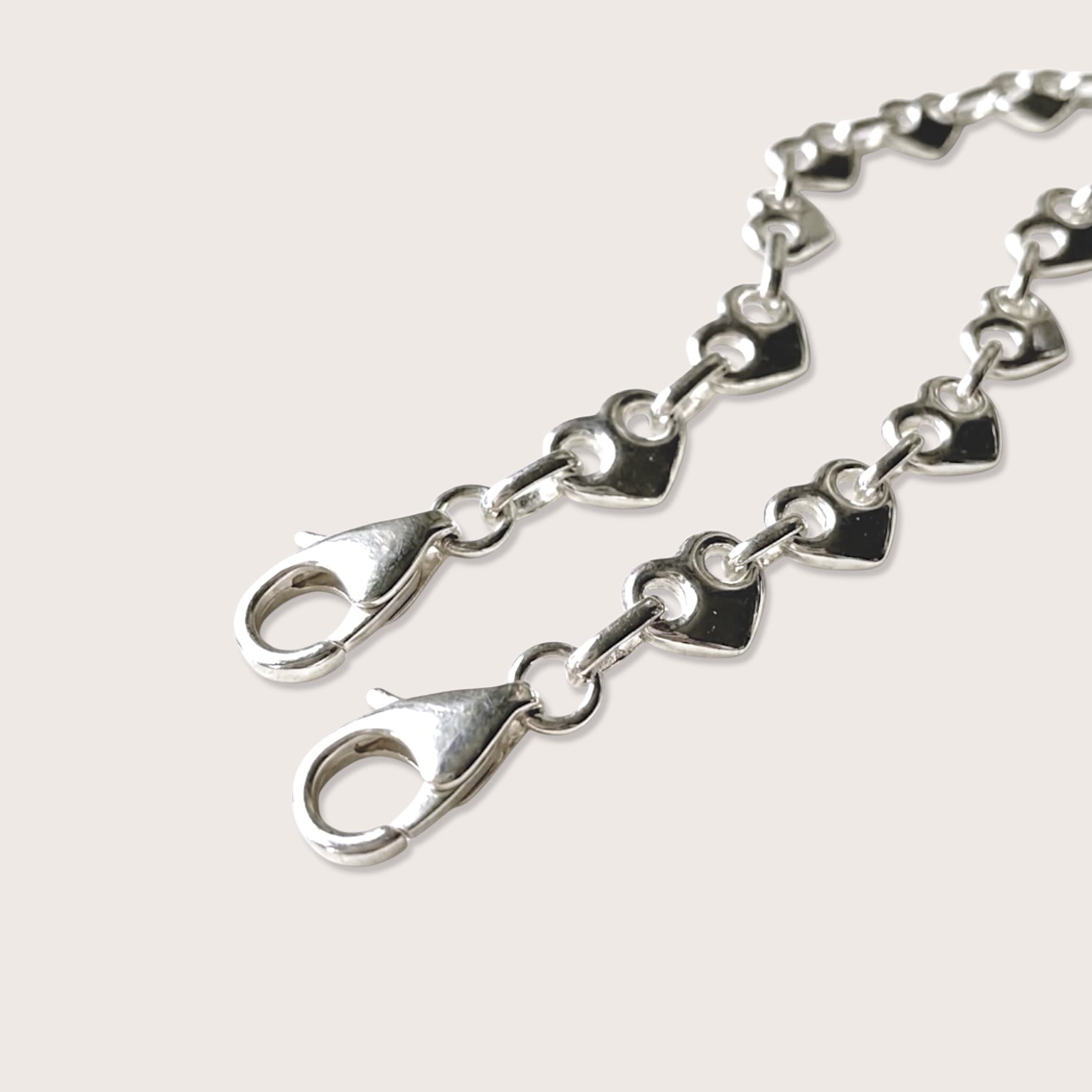 A close up image of a chunky solid silver puffed heart mariner bracelet on a plain background focused on the lobster clasp closure and the heavy weight link chain