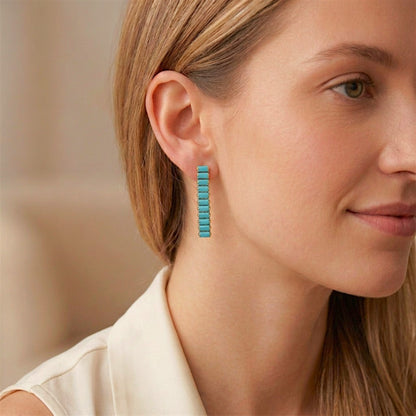 Close-up of a woman wearing a turquoise-blue baguette drop earring with gold-tone settings.