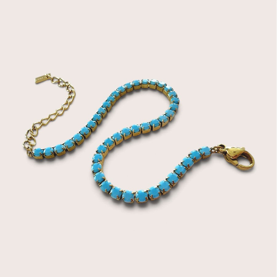 Close-up view of the secure 4-prong setting and vibrant teal crystal stones on a waterproof gold bracelet.