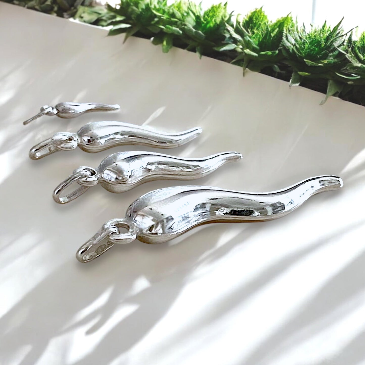 lose-up shot highlighting the high-shine mirror finish and twisted dimensional curves of the sterling silver cornicello charms resting under soft studio light.
