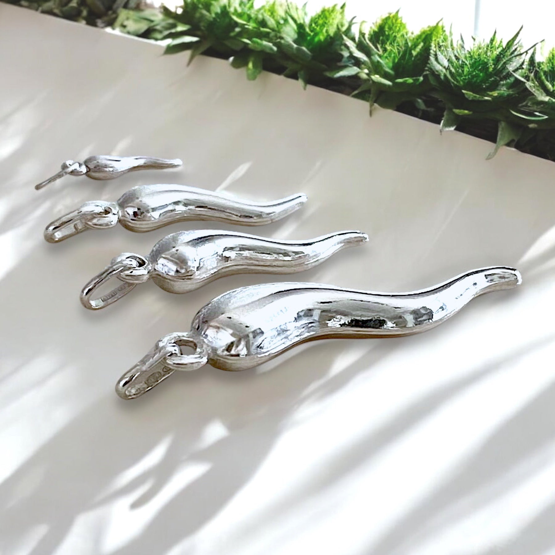 lose-up shot highlighting the high-shine mirror finish and twisted dimensional curves of the sterling silver cornicello charms resting under soft studio light.