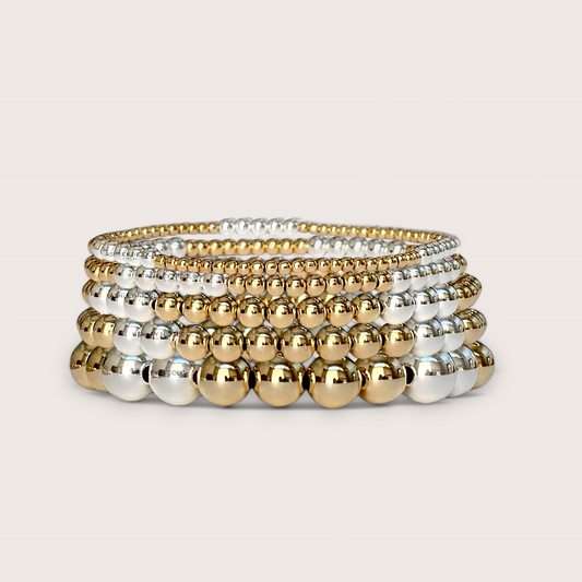 An alternating 14K gold-filled and 925 sterling silver two-tone mixed metal beaded stretch bracelets stacked showcased on a clean white background.