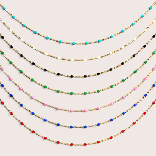 Six gold-filled enamel station necklaces in turquoise, black, green, pink, blue, and red arranged on a light background by Ashley Nicole Jewelry