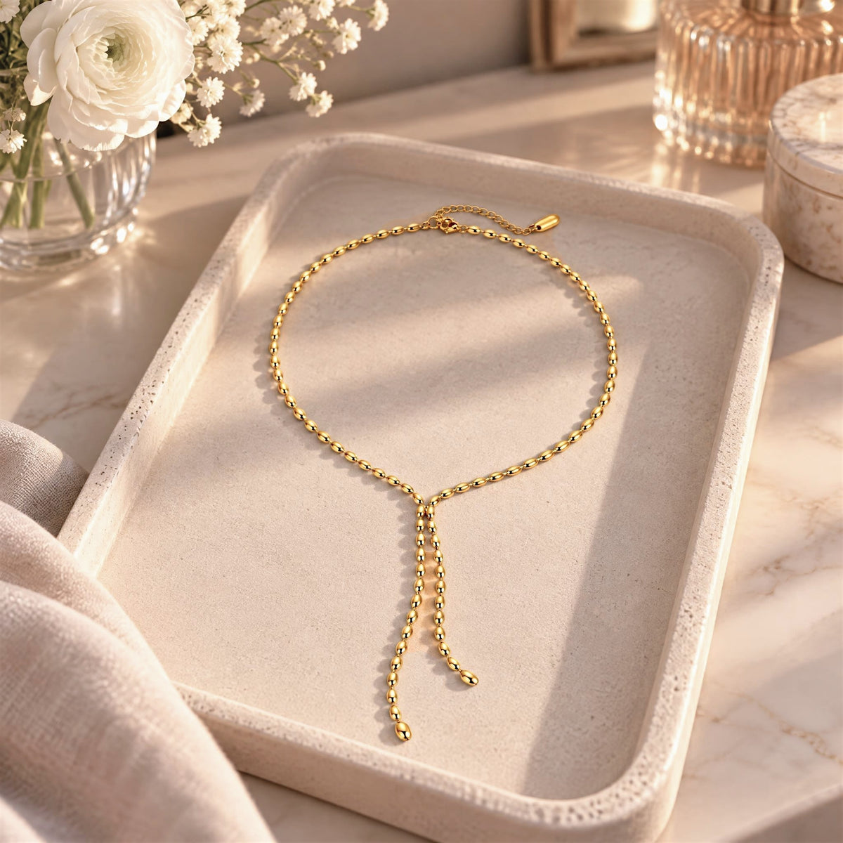 Detailed view of the 18K gold PVD beaded chain and Y-drop on a light background